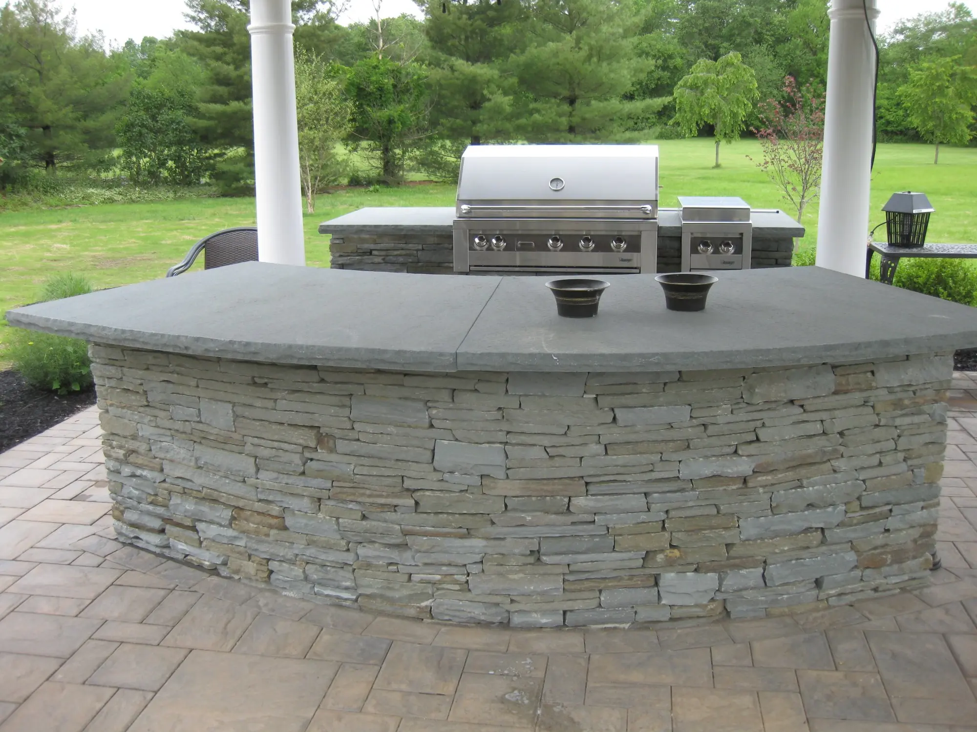 Stone outdoor kitchen with stainless steel grill under pergola